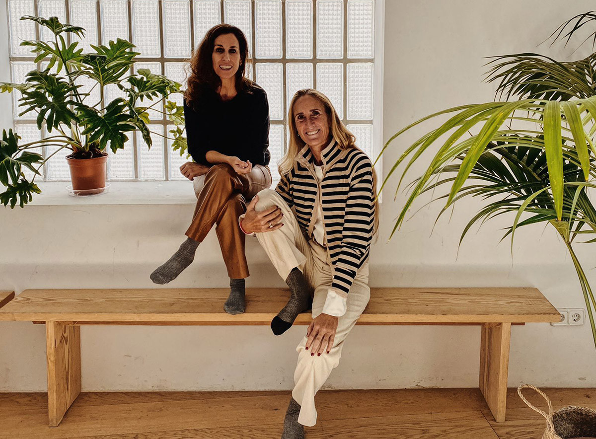 Mercedes de la Rosa and Cristine Bedfor sitting on a wooden bench.